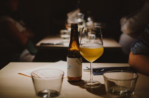 Taça de cerveja e uma garrafa em mesa de restaurante. Foto: Pille Riin Priske via Unsplash