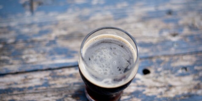 Pint de cerveja escura em uma mesa de madeira. Foto: Amy Parkes via Unsplash