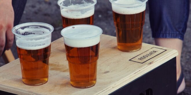 4 copos de cerveja de cor âmbar em copos de plástico transparentes. Foto: Julia Nastogadka via Unsplash