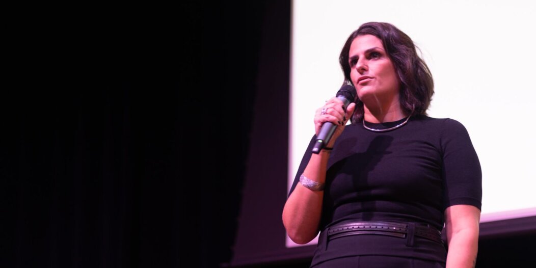 Mulher vestida de preto pose confiante com microfone falando em um evento